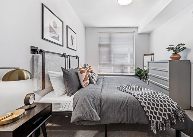 Modern bedroom with a queen-size bed, gray bedding, decorative pillows, and artwork on the wall.