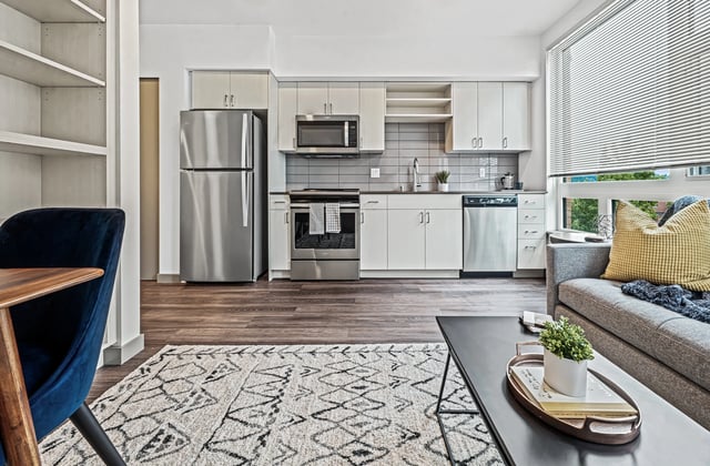 Modern apartment kitchen and living area with stainless steel appliances, white cabinets, and a sofa.