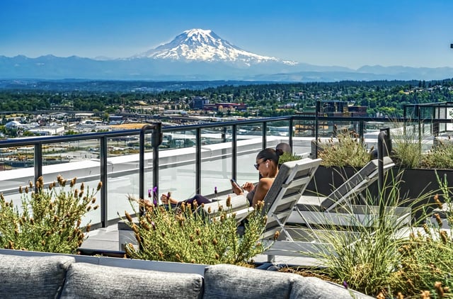 Woman relaxing on a lounge chair on a balcony overlooking a cityscape and mountains.
