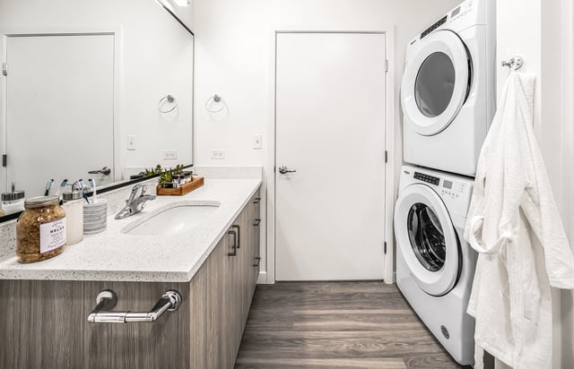Modern bathroom with a sink, vanity, stacked washer and dryer, and a fluffy white robe hanging.