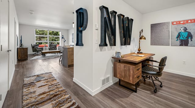 Stylish home office with a rustic wooden desk and black leather chair next to a living area.