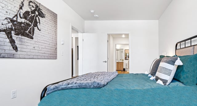 Bedroom with a large teal bed, decorative pillows, and Banksy-style artwork on the wall.