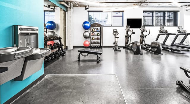 Modern fitness center with treadmills, ellipticals, free weights, and a water fountain.
