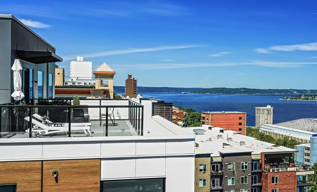 Rooftop deck with lounge chairs and a view of the water and distant hills.