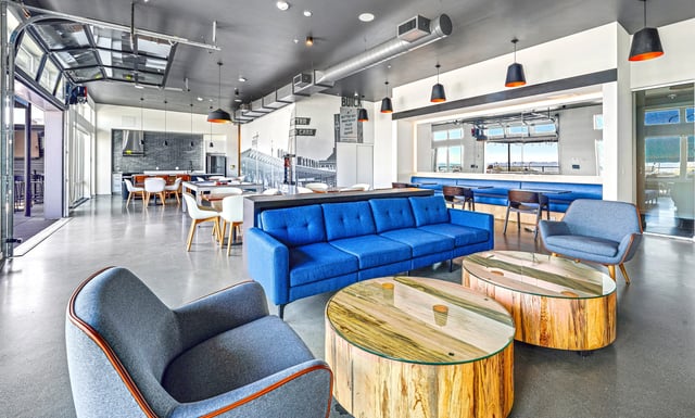 Modern communal lounge with blue couches, armchairs, and rustic coffee tables.