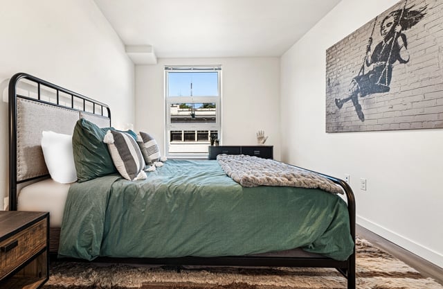 Bedroom with a queen bed, green bedding, and modern art on the wall.