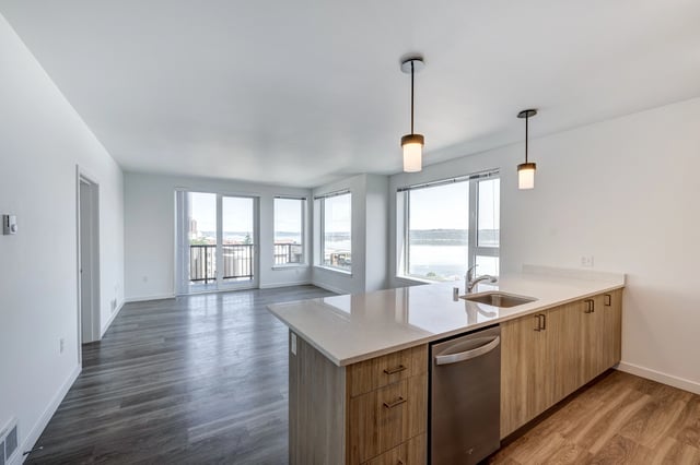 Modern apartment kitchen with island and stainless steel appliances, overlooking water view.