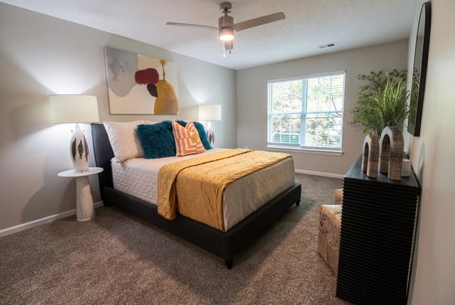 A master bedroom with a queen-size bed, a ceiling fan, and a large window.