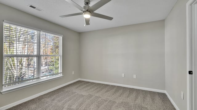 Empty bedroom with neutral carpet, a ceiling fan, and a large window with blinds.