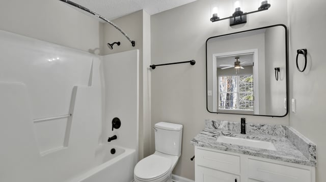 Clean and modern bathroom with white bathtub, toilet, and vanity with granite countertop.