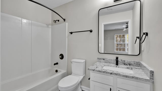 Clean and modern bathroom with a white tub, toilet, and vanity with a granite countertop.