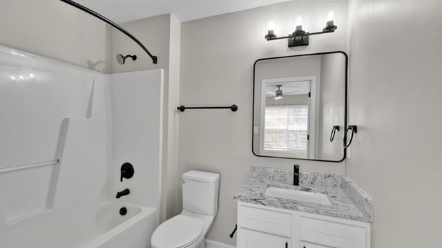 Modern bathroom with a white bathtub, toilet, vanity, and black fixtures.