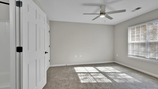 Bedroom with neutral gray walls, carpet, ceiling fan, and blinds.