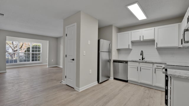 Modern kitchen with white cabinets, granite countertops, stainless steel appliances, and an open view to the living area.