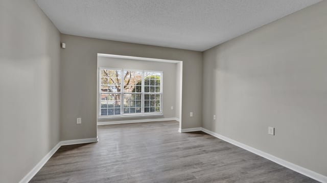 Empty living room with large windows overlooking trees.