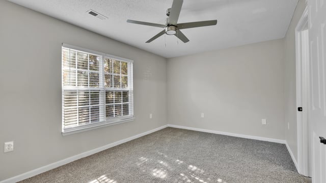 Bedroom with neutral gray walls, carpet, a ceiling fan, and a large window with blinds.