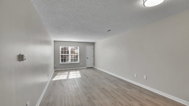 Empty living room with gray walls, wood laminate flooring, and a window with blinds.