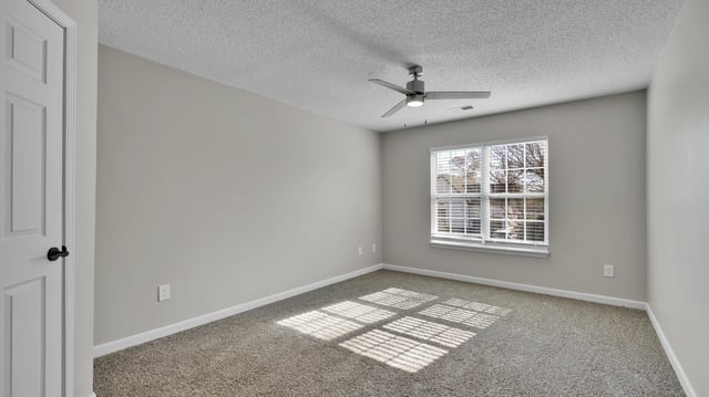 Empty bedroom with a white door, ceiling fan, and window.