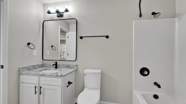 Modern bathroom with granite vanity, modern toilet, and white bathtub.