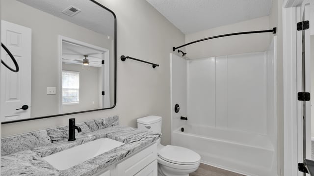 Modern bathroom with granite vanity, black fixtures, and white bathtub and toilet.