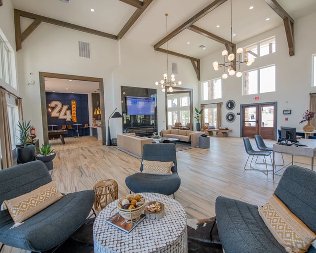 Bright community lounge with high vaulted ceiling, wooden beams, chandeliers, and seating area.