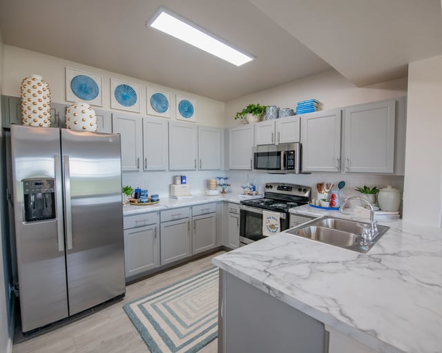 Modern kitchen with gray cabinets, marble countertops, and stainless steel appliances.