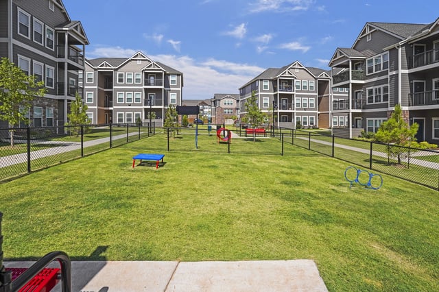 Fenced community courtyard with lawn, playground equipment, and multi-story apartment buildings.