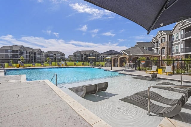 Outdoor swimming pool with lounge chairs and surrounding apartment buildings.