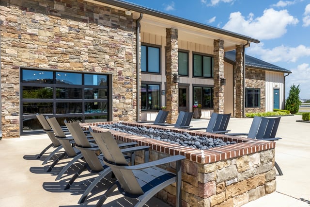 Outdoor fire pit with lounge chairs in front of a building with stone accents and large windows.