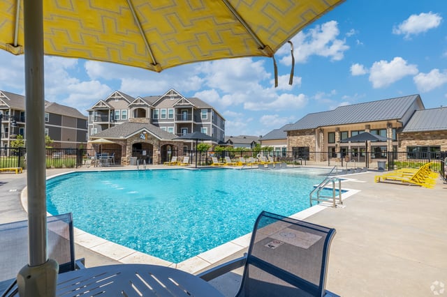 Resort-style swimming pool with lounge chairs and umbrellas. Buildings and clubhouse in background.