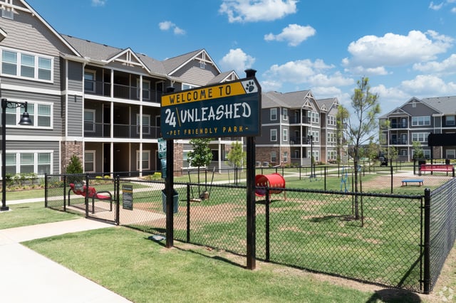 Welcome to 24 Unleashed pet friendly park sign with apartment buildings in the background.