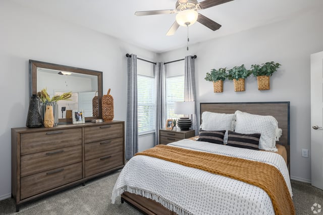 Queen-size bed with white bedding and a burnt orange throw blanket, nightstand, dresser with mirror, and ceiling fan.