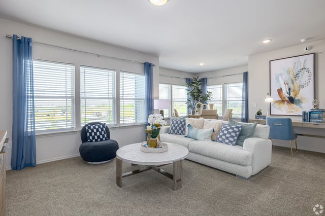 Spacious living room with a white sofa, coffee table, desk, and large windows.