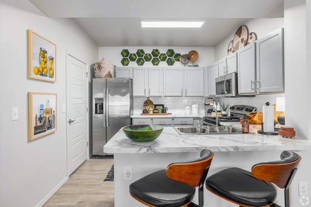 Modern apartment kitchen with stainless steel appliances, white cabinets, and a marble countertop.