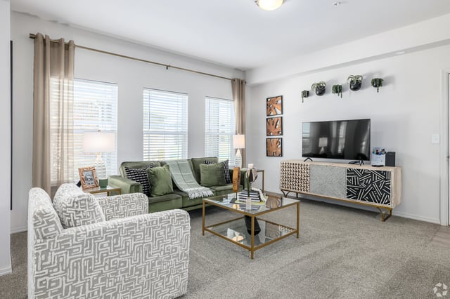 Modern living room with a green sectional sofa, patterned accent chairs, a glass coffee table, and a TV.