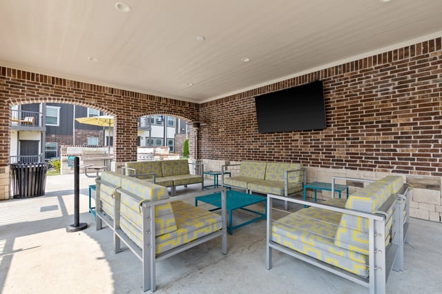 Covered outdoor lounge area with sofas, chairs, coffee tables, and a TV.