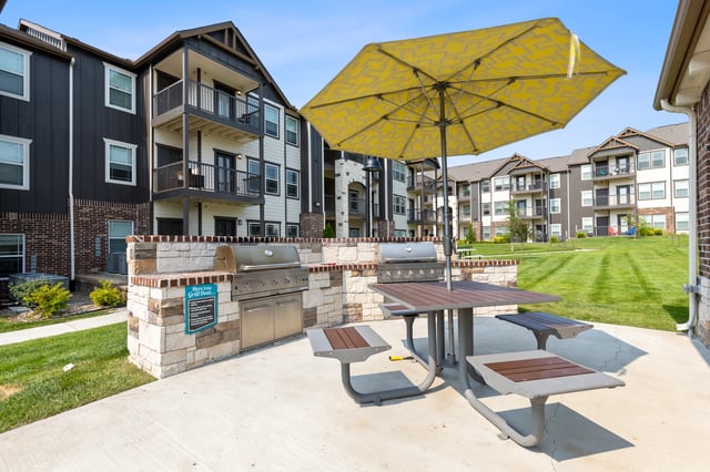 Outdoor grilling station with two built-in grills and a picnic table with umbrella.