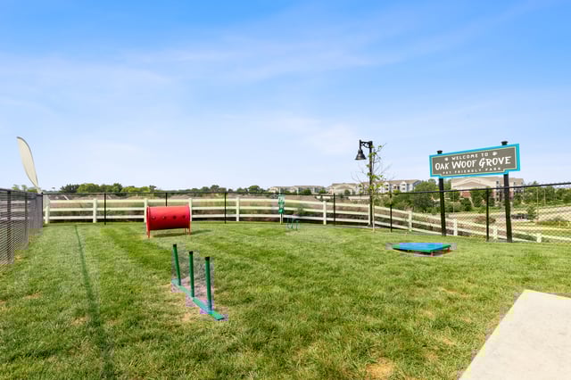 A fenced-in dog park with agility equipment and a welcome sign.