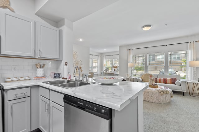 Modern kitchen with marble countertops and stainless steel appliances, opens to a living area.