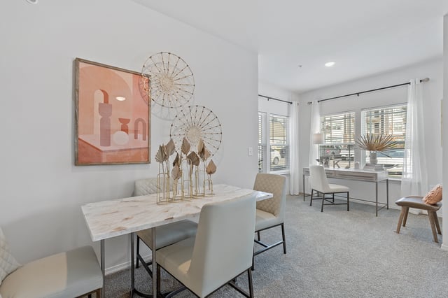 Dining area with a marble table and chairs, adjacent to a workspace with a desk and chair.