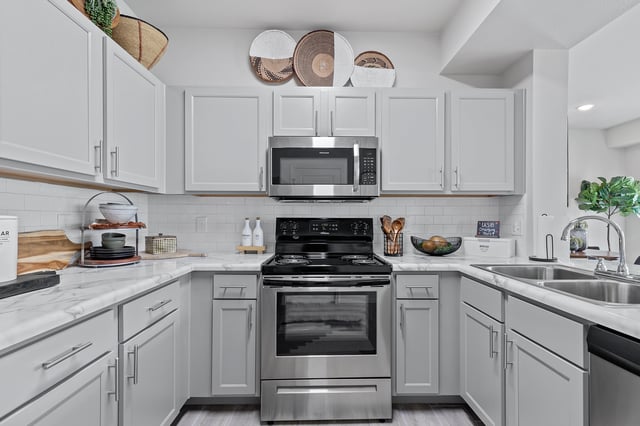 Modern kitchen with light grey cabinets, stainless steel appliances, and marble countertops.