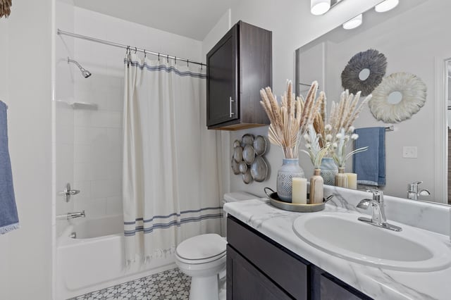 Modern bathroom with a white tub, shower curtain, toilet, and vanity with a marble countertop.