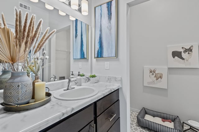 Bathroom vanity with marble countertop, sink, faucet, mirror, and decorative items.