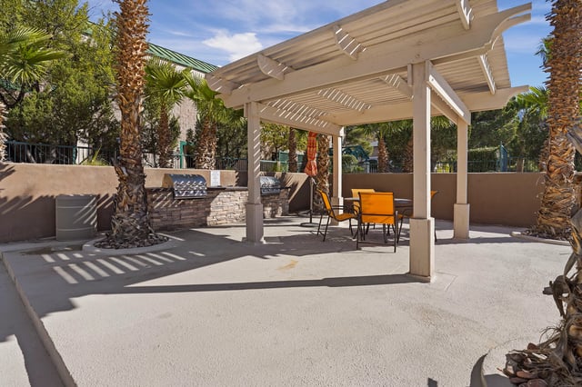 Outdoor grilling area with two built-in grills and a picnic table under a pergola.