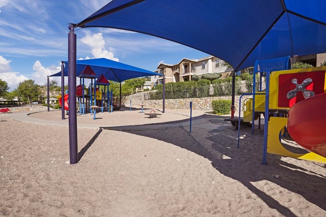 Playground area with slides, swings, and a see-saw under blue canopies.