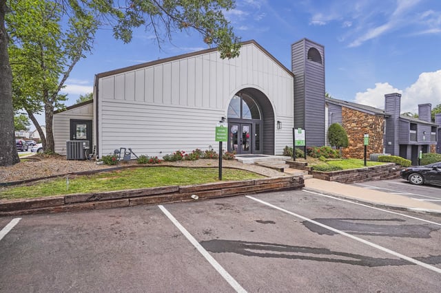 Exterior view of a multifamily community building with an arched entry and parking area.