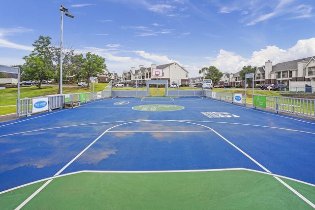 Outdoor blue basketball court with hoop, fenced, at a multifamily community.