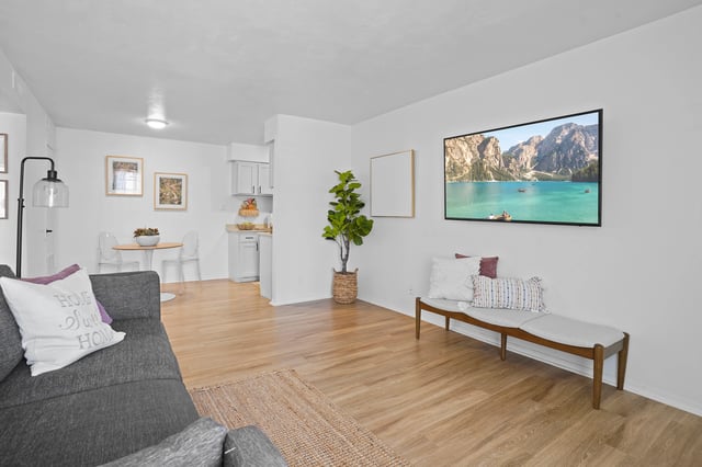 Modern living room with a dark gray sofa, bench, and large TV displaying a mountain lake scene.