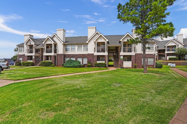 Exterior view of apartment buildings with manicured lawns and trees.