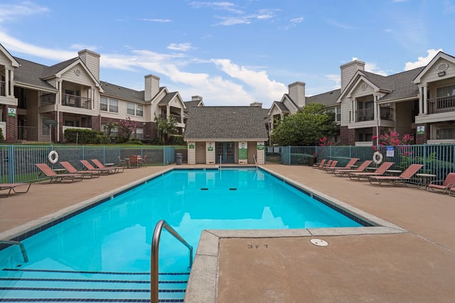 Apartment complex pool with lounge chairs and buildings in the background.